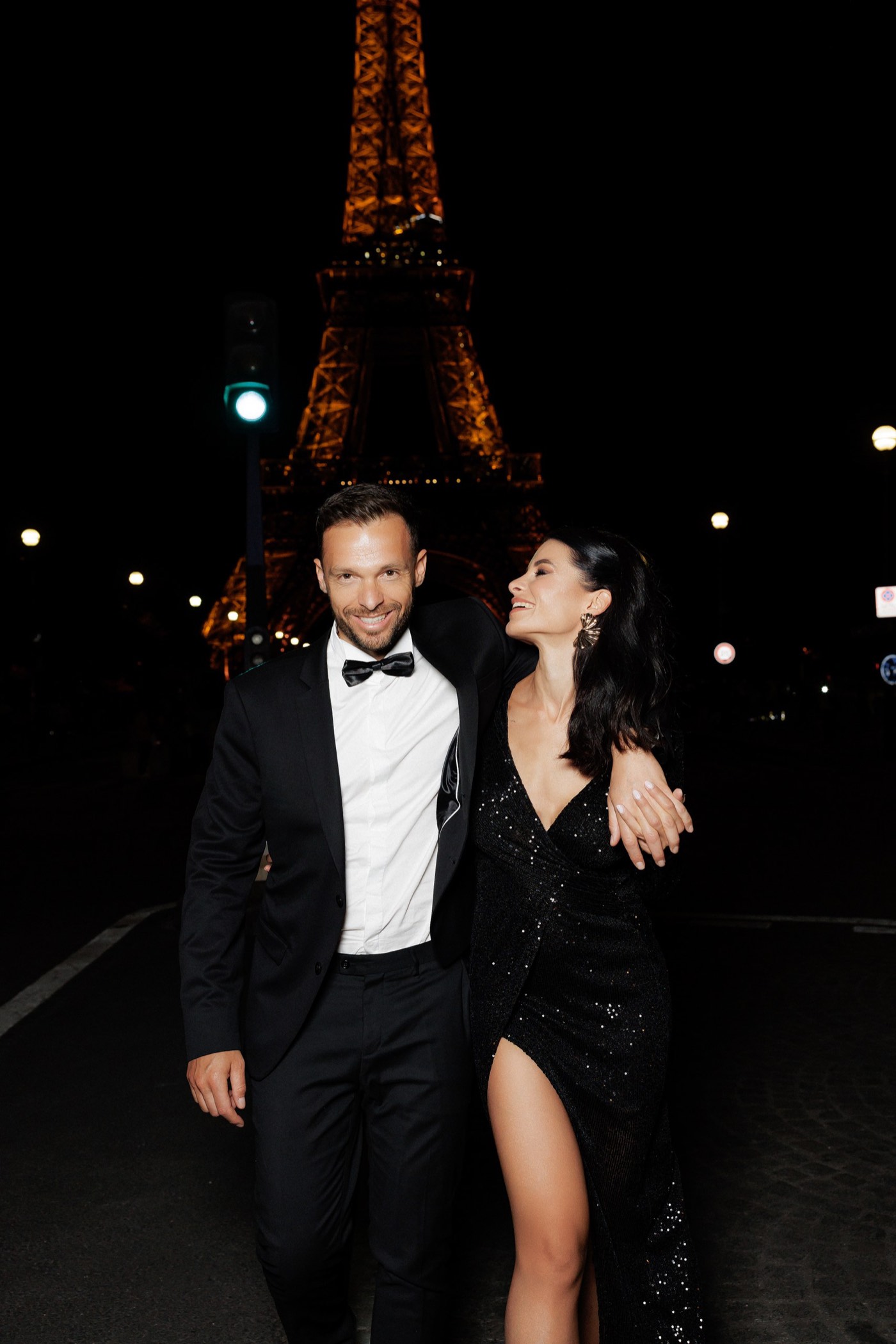 Couple laughing together at night in front of the illuminated Eiffel Tower